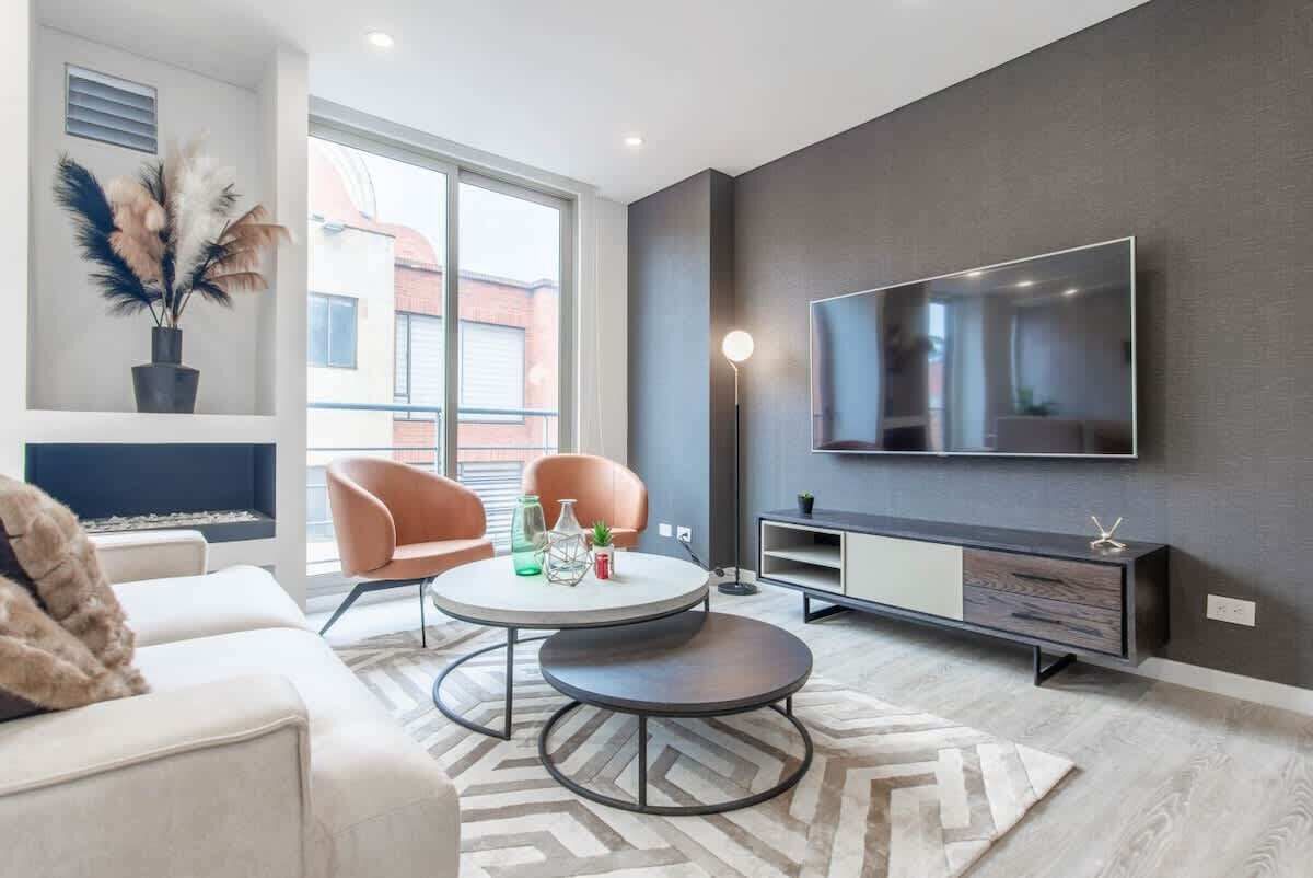 Ein stilvolles Wohnzimmer mit einer Couch, zwei Sesseln, einem runden Couchtisch, einem flachbildfernseher an der Wand, einer Anrichte und einer Topfpflanze.