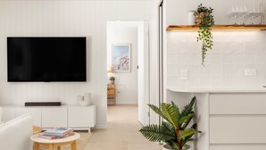 A modern living room with a flat-screen TV, white furniture, a small table with books, and a potted plant. - Solara Escape Mooloolaba, Pool + Dog-Friendly Home (Mooloolaba Region)