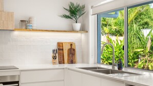 A modern kitchen with white cabinets, a dishwasher, and a window with a view of greenery. - Solara Escape Mooloolaba, Pool + Dog-Friendly Home (Mooloolaba Region)