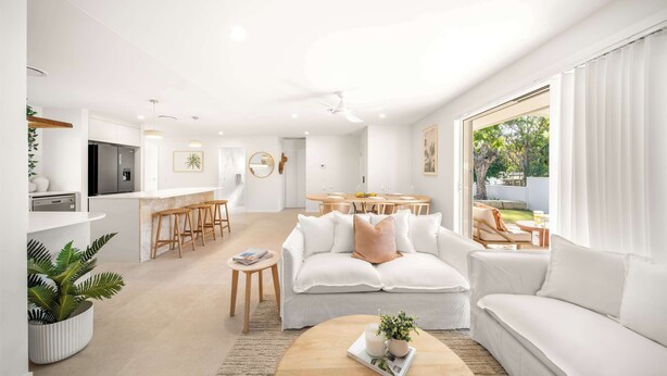 A modern living room with a white sofa, a coffee table, and a dining area with a table and chairs. - Solara Escape Mooloolaba, Pool + Dog-Friendly Home (Mooloolaba Region)