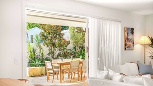 A room with a bed, a table, and chairs, a sliding glass door leading to an outdoor area with plants and a table set for dining. - Solara Escape Mooloolaba, Pool + Dog-Friendly Home (Mooloolaba Region)
