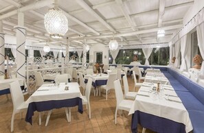 A restaurant with white tables and chairs, blue tablecloths, and a view of the outdoors. - Hotel Tritone Resort AND SPA (Forio)
