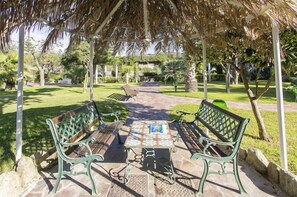 A covered outdoor seating area with benches and a table, surrounded by greenery and a pathway. - Hotel Tritone Resort AND SPA (Forio)