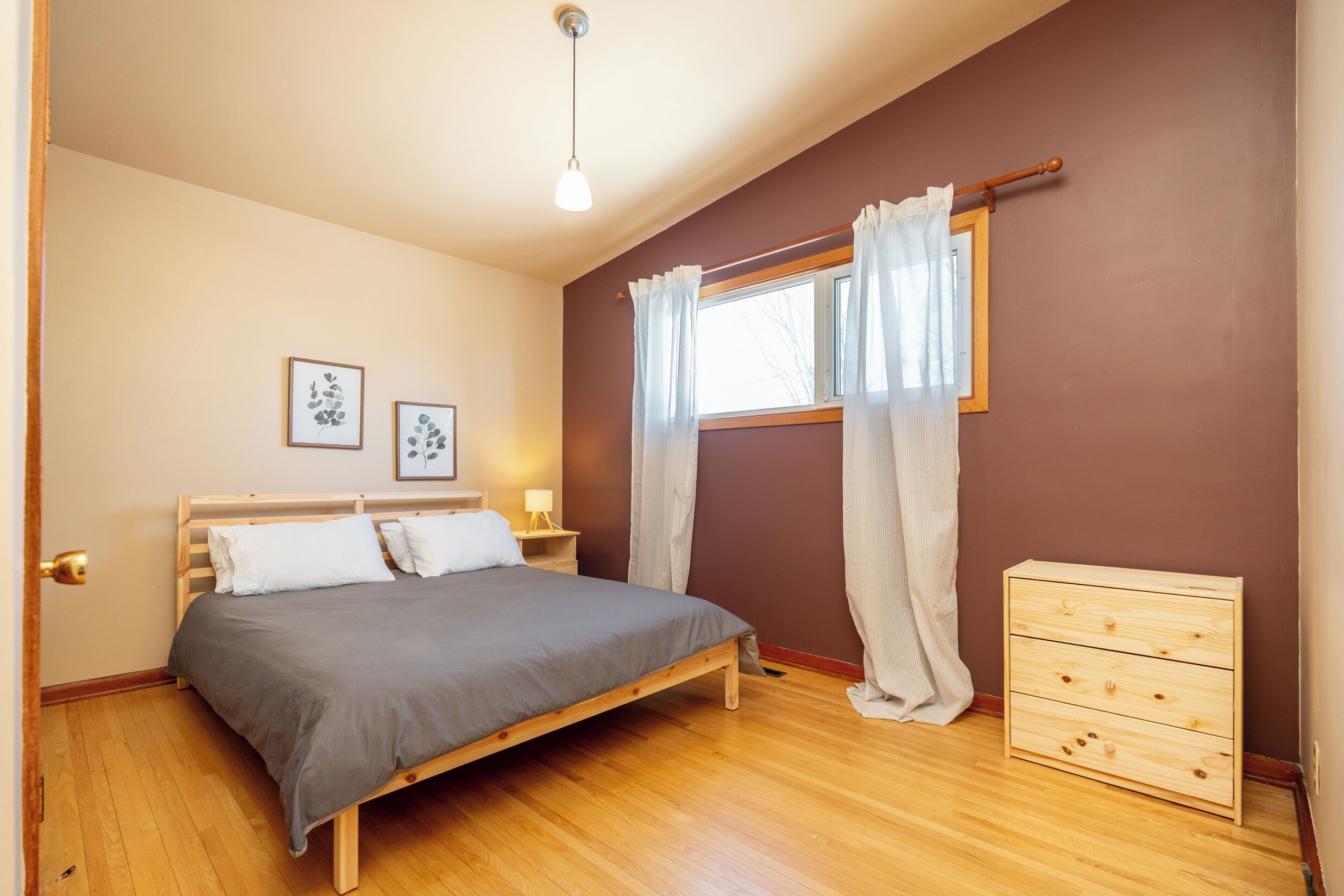 Una camera da letto con un letto in legno, un comodino, una cassettiera e una finestra con tende.