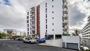 A modern multi-story residential building with balconies, a parking area with several cars, and a clear sky. - Camélia's Apartment I –  Modern in Funchal (Funchal)