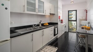 A modern kitchen with white cabinets, a black countertop, and a view of the outside through a glass door. - Camélia's Apartment I –  Modern in Funchal (Funchal)