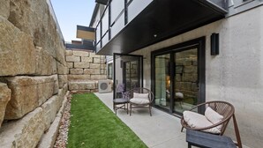 Un patio moderno al aire libre con muros de piedra, un pequeño césped y dos sillas de mimbre.