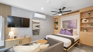 Una habitación de hotel moderna con cama, escritorio, silla, televisor y ventilador de techo.