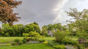 Ein Haus, umgeben von einem üppigen Garten mit verschiedenen Pflanzen und Bäumen.