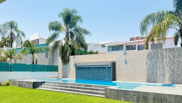 A modern outdoor swimming pool with a stone wall and palm trees. - Luxury home for 25, Lomas de Cocoyoc, swimming pool, jacuzzi, private garden (Fraccionamiento Lomas de Cocoyoc)