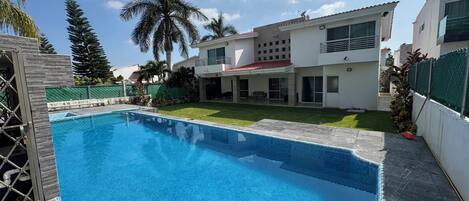 A swimming pool with a tiled edge, surrounded by a well-maintained lawn and palm trees.