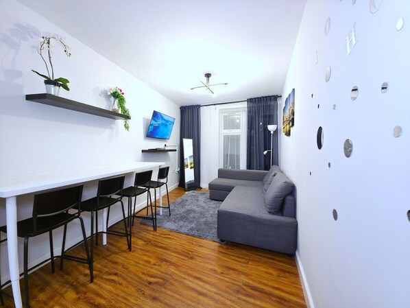 A modern living room with a grey sofa, a dining table with chairs, a TV, and a ceiling fan.