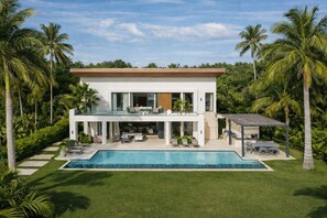 Ein modernes, zweistöckiges Haus mit Swimmingpool, umgeben von Palmen und viel Grün.
