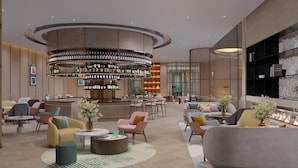 Um saguão de hotel moderno com um bar central, áreas de estar e um lustre decorativo.