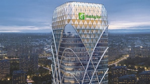 Um Holiday Inn imponente com fachada de vidro geométrica marcante, diante de um horizonte urbano ao entardecer.