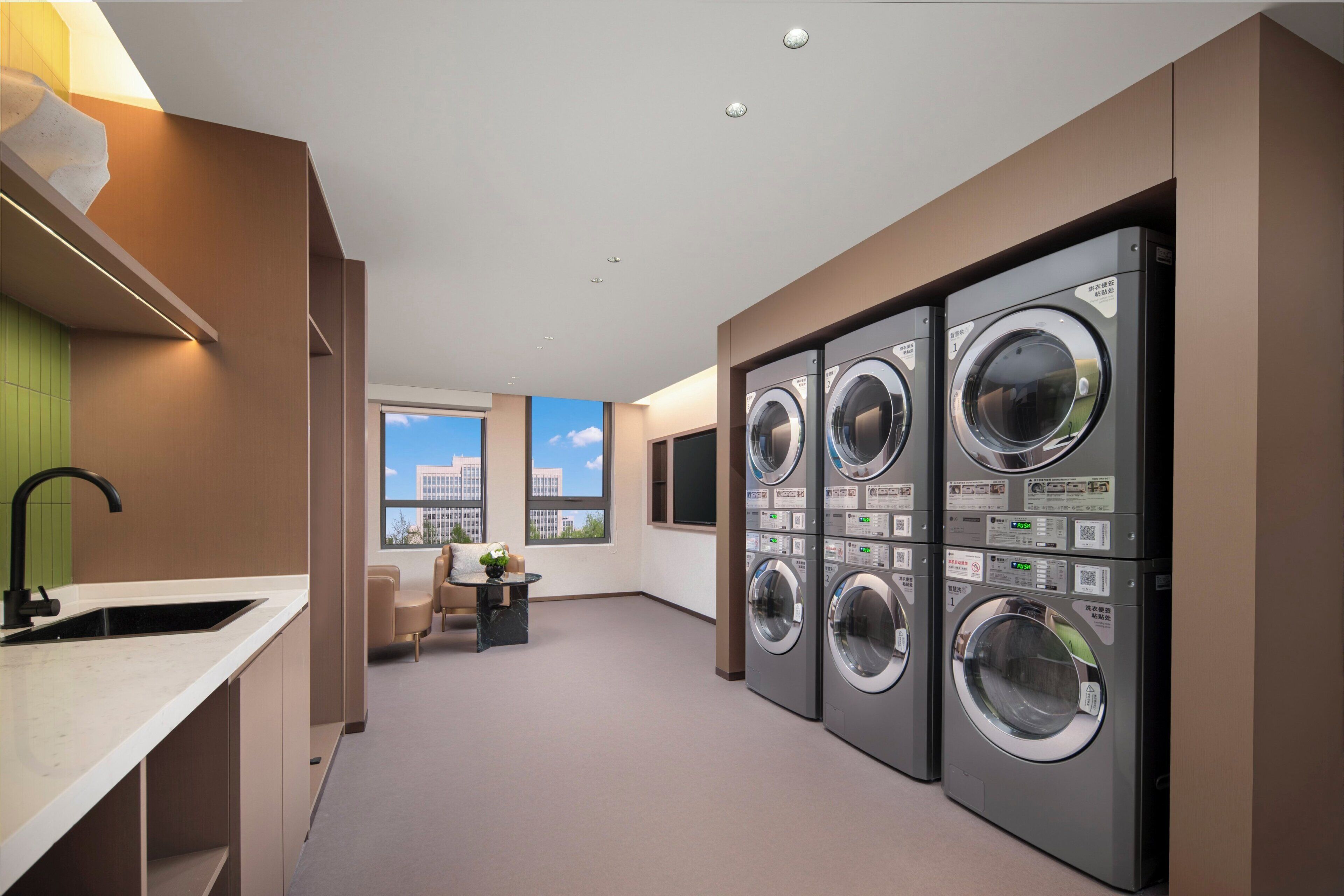 A laundry room with multiple washing machines, a sink, and a window with a view.