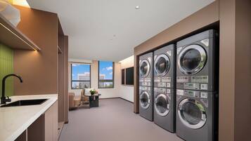 A laundry room with multiple washing machines, a sink, and a window with a view.