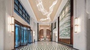 Un'ampia hall con pavimento a motivi geometrici, una grande parete in marmo e un'originale lampada a sospensione.