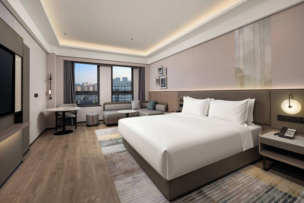 Una habitación de hotel moderna con una cama grande, zona de estar, escritorio y vistas a la ciudad.