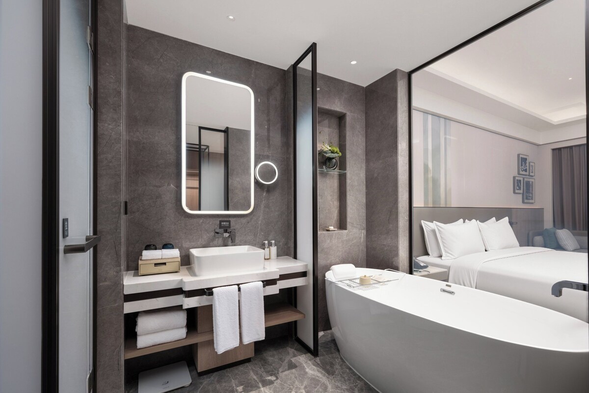 A modern bathroom with a large mirror, a bathtub, and a vanity with a sink and towel rack.