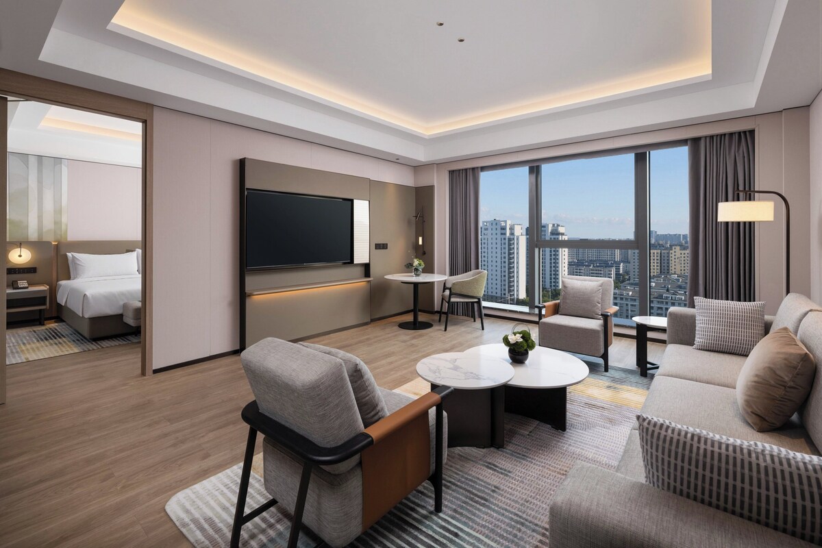 A modern hotel room with a large bed, a TV, a dining area, and a sofa.