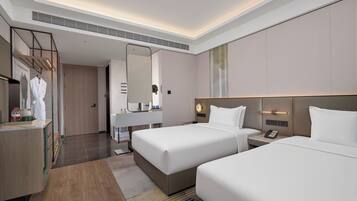 A hotel room with two beds, a vanity with a mirror, a robe hanging, and a bedside table with a phone.