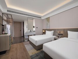 A hotel room with two beds, a vanity with a mirror, a robe hanging, and a bedside table with a phone.