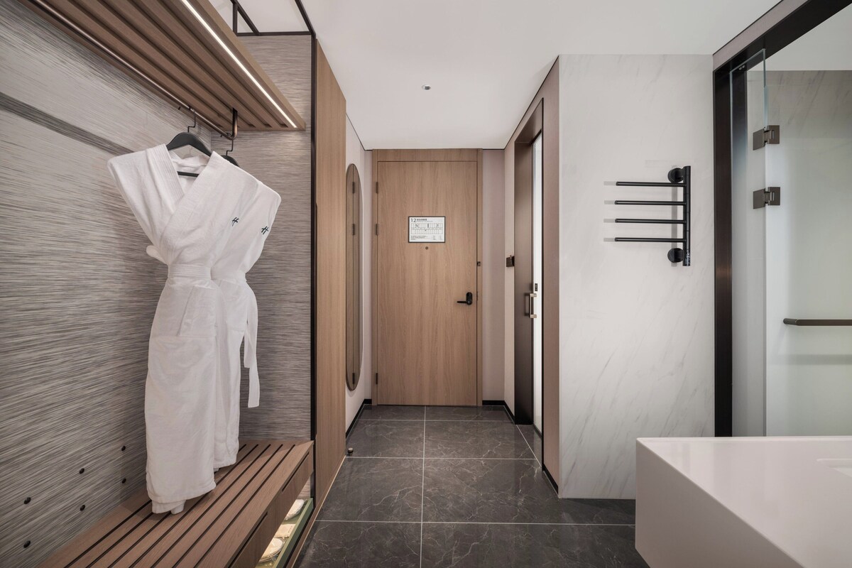 A modern hotel corridor with a wooden bench, a robe hanging on the wall, and a door with a sign.