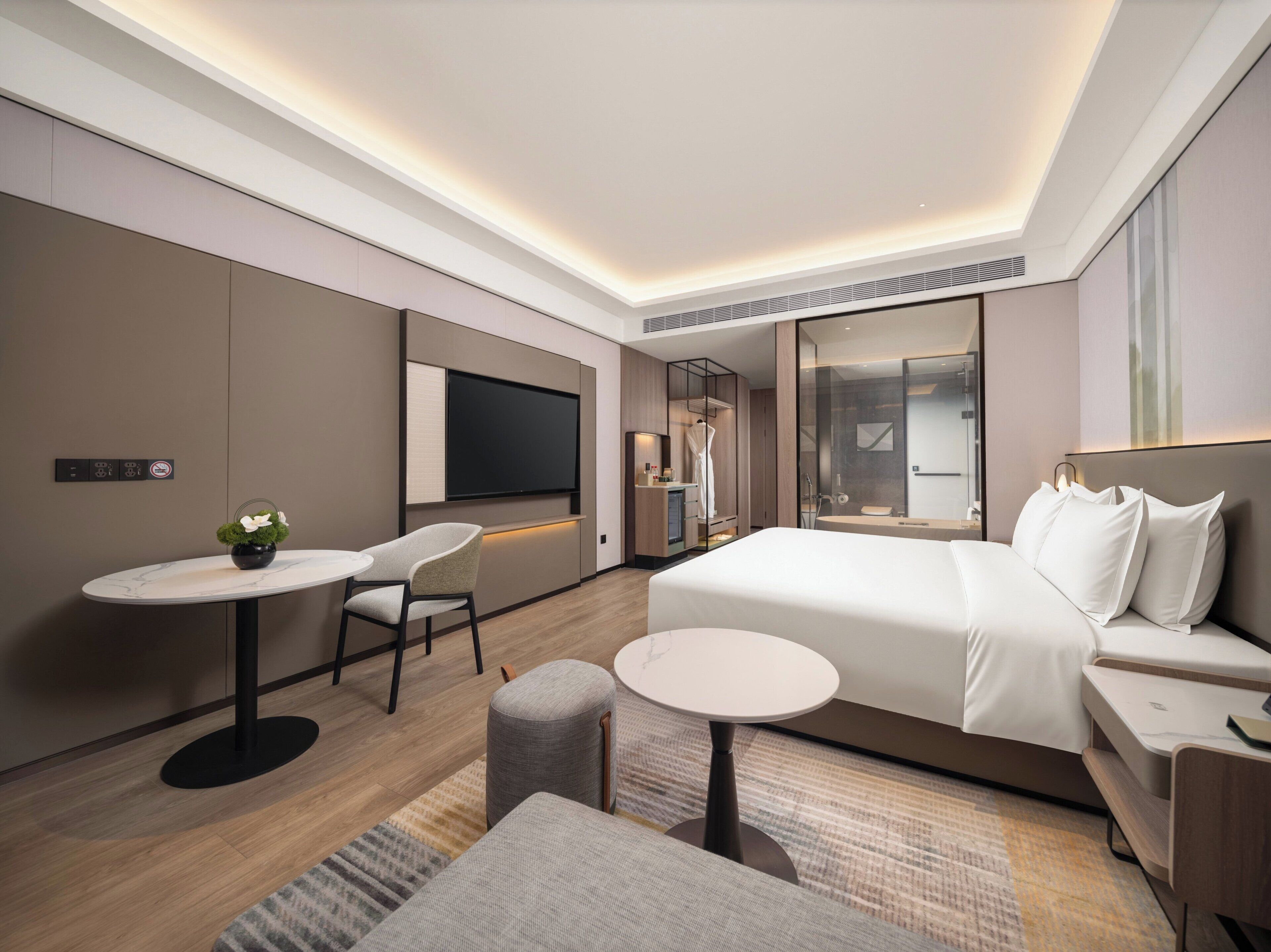 Una habitación de hotel moderna con cama, televisor, una mesita y un rincón de descanso.