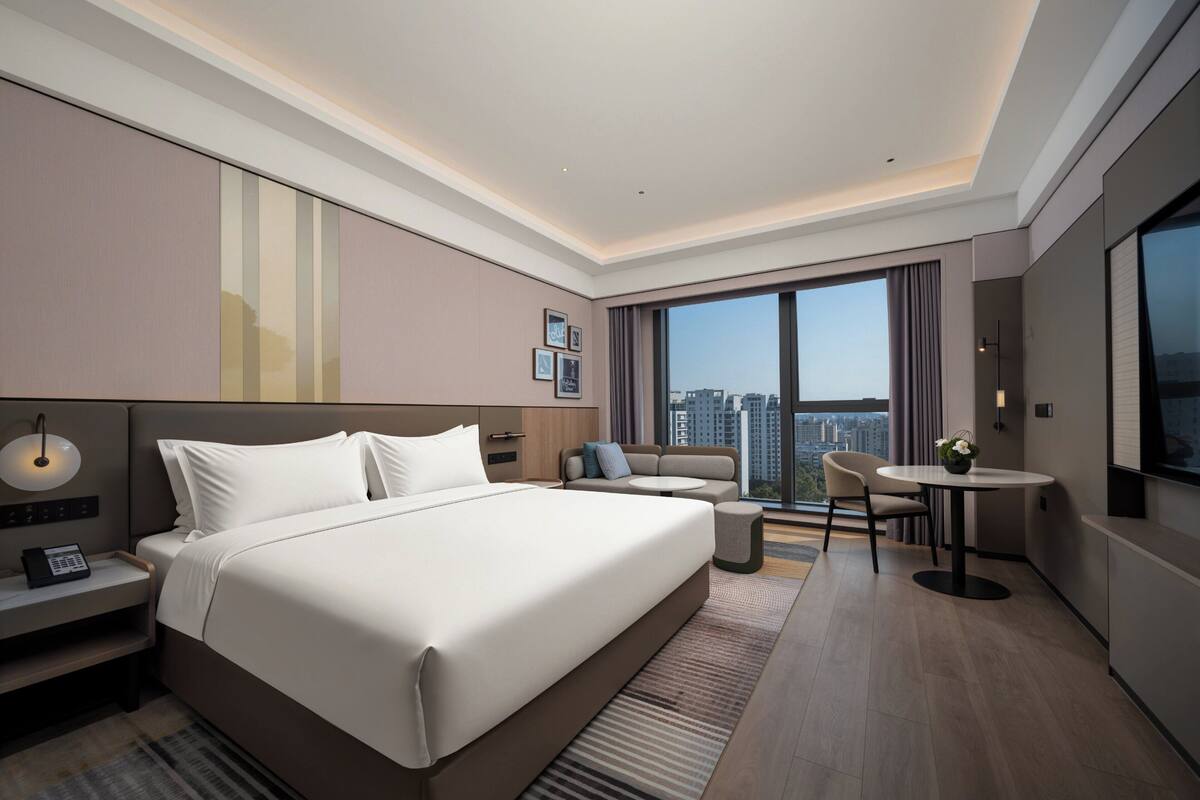 Una habitación de hotel moderna con una cama grande, un escritorio, una silla y vistas de la ciudad.