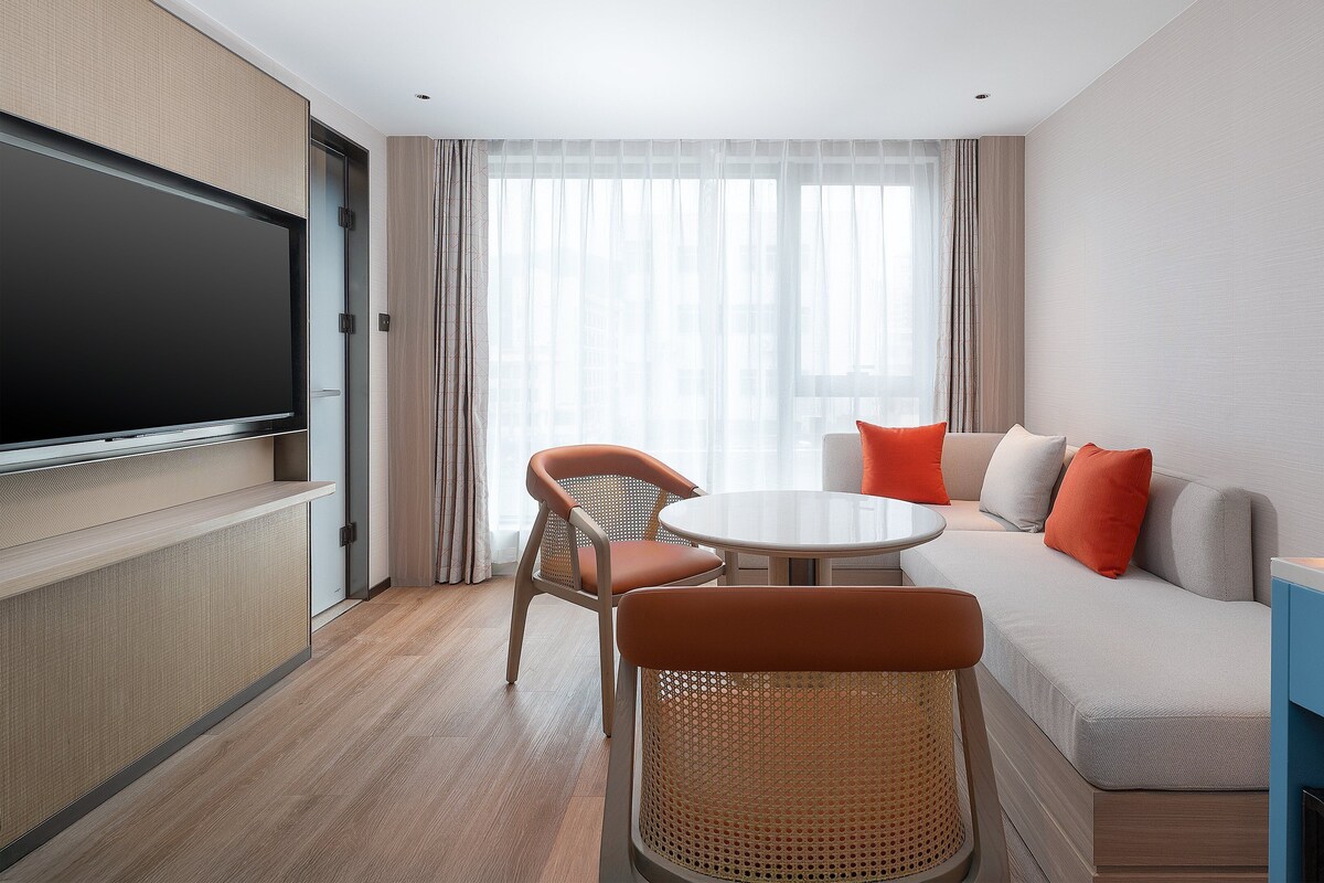 Habitación de hotel con televisión de pantalla plana, un sofá, dos sillones, una mesita redonda y una cafetera.