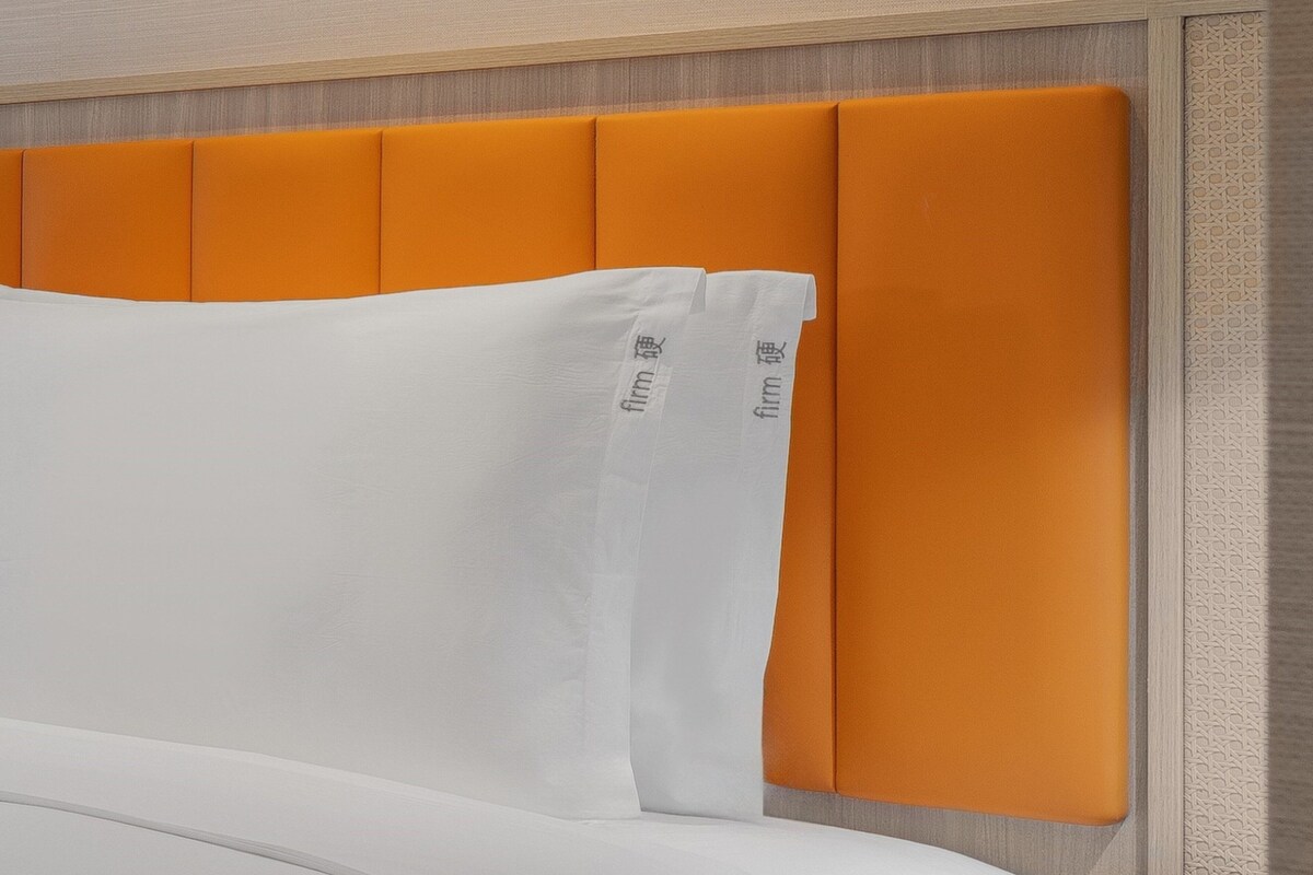 Una cama con cabecera naranja y almohadas blancas.