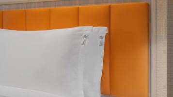 A bed with an orange headboard and white pillows.