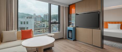 Ein Hotelzimmer mit großem Fenster, einem Bett, einem Fernseher, einem kleinen Tisch und einer Sitzecke.