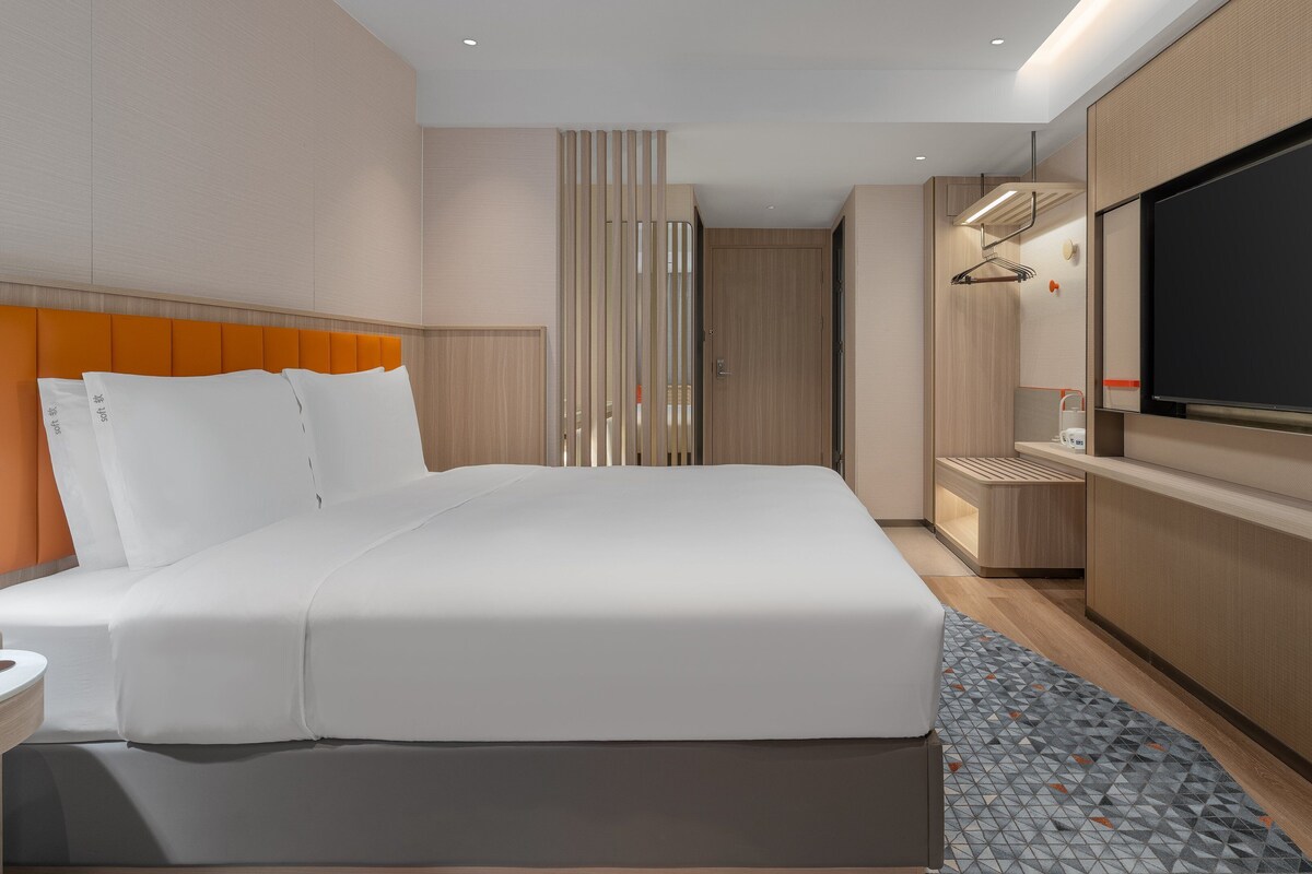 A modern hotel room with a large bed, a television, a desk, and a bathroom.