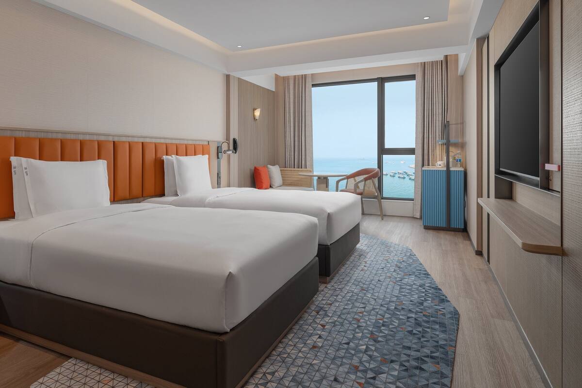 Une chambre d’hôtel avec deux lits, une télévision, une vue sur la mer et un balcon.