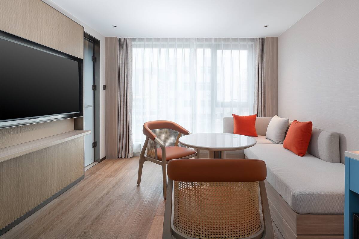 Une chambre d’hôtel équipée d’un téléviseur à écran plat, d’un canapé, de deux fauteuils, d’une petite table ronde et d’une machine à café.