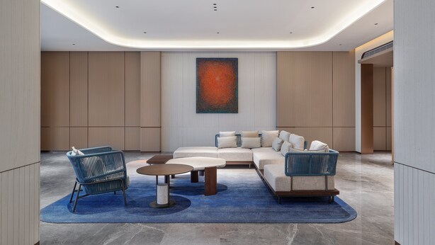 Un salon moderne avec un canapé d’angle, deux fauteuils, une table basse et un grand tableau abstrait accroché au mur.