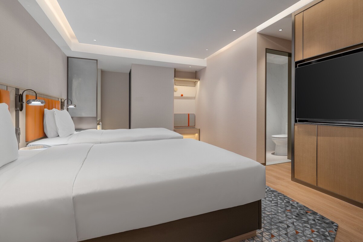 A modern hotel room with a large bed, a flat-screen TV, and a bathroom visible through an open door.