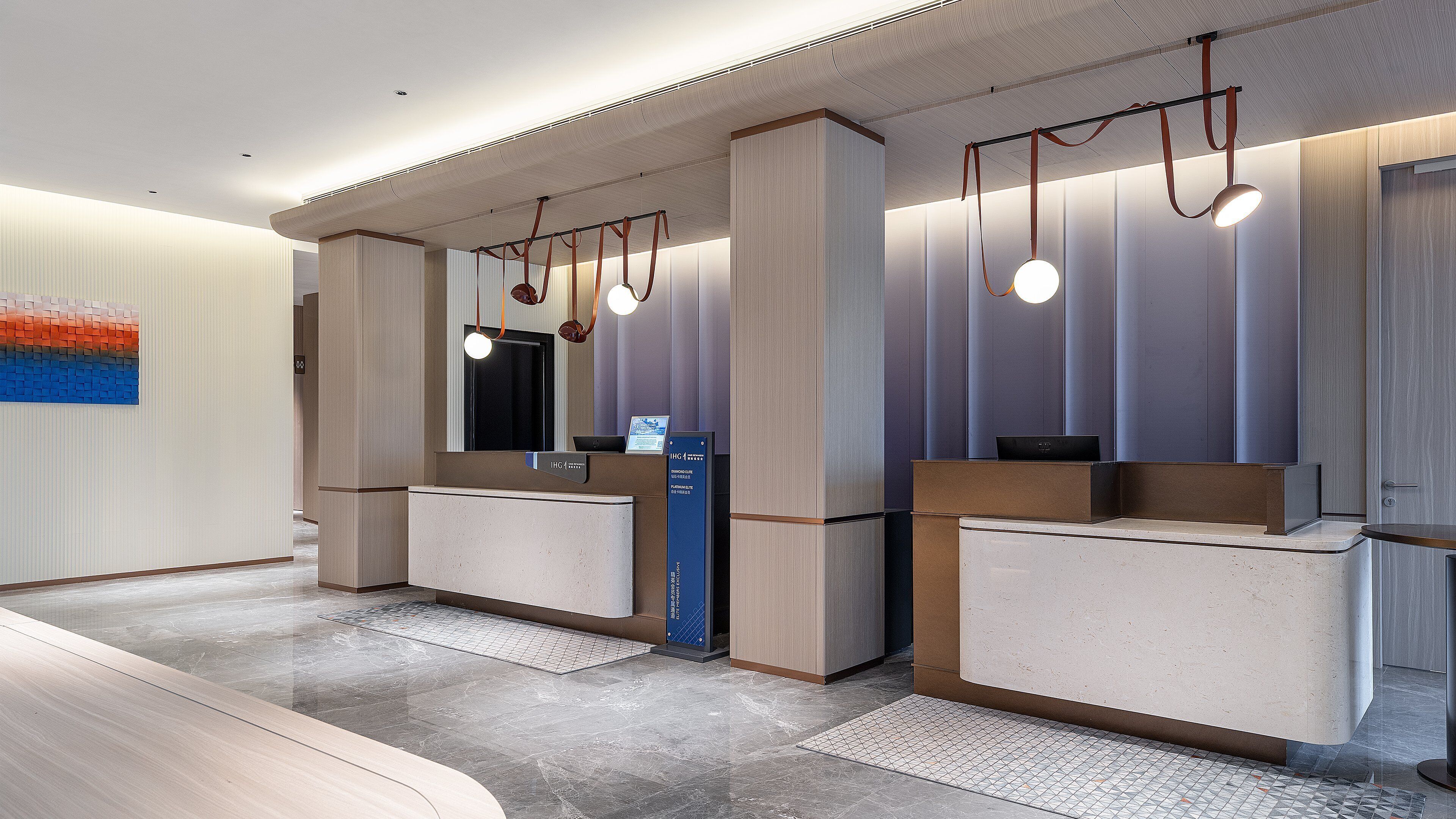 A modern hotel reception area with a counter, a large mirror, and pendant lighting.
