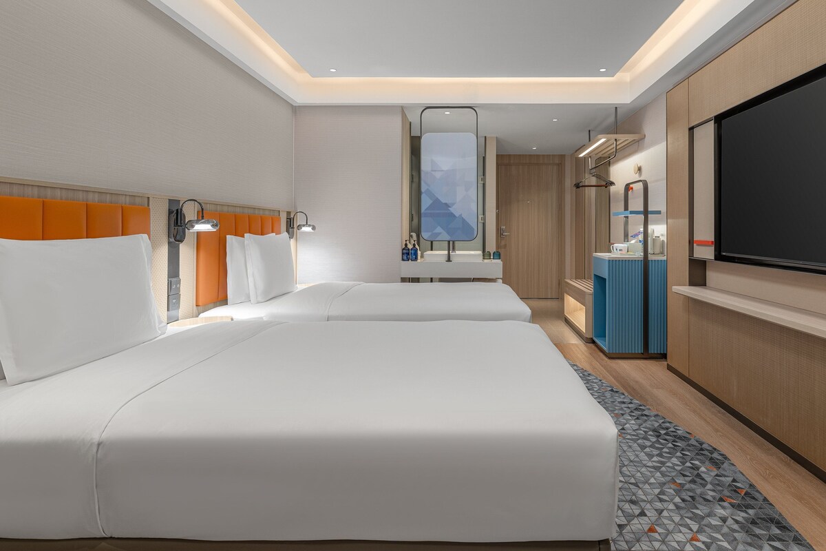 A hotel room with two beds, a TV, a minibar, and a bathroom.