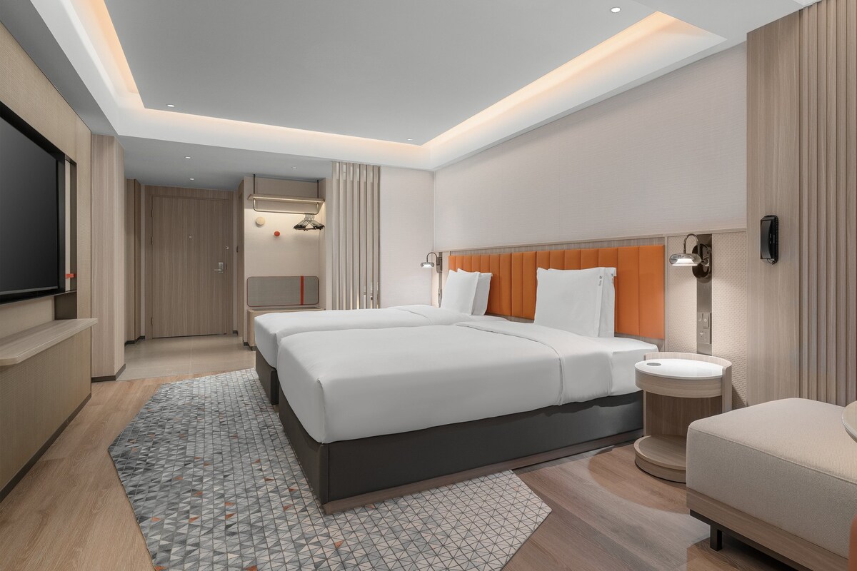 A modern hotel room with a large bed, a bedside table, a TV, and a bathroom with a shower.