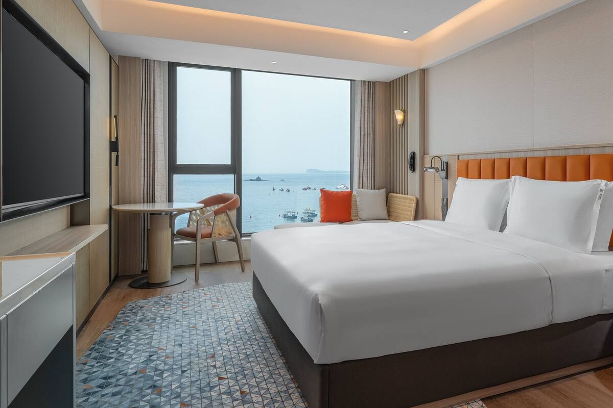 Une chambre d’hôtel équipée d’un lit, d’un bureau, d’une chaise, d’une télévision et offrant une vue sur la mer.