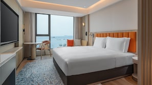 A hotel room with a bed, a desk, a chair, a TV, and a view of the sea. - Holiday Inn Express Shenzhen Dapeng Nan'ao by IHG (Shenzhen)