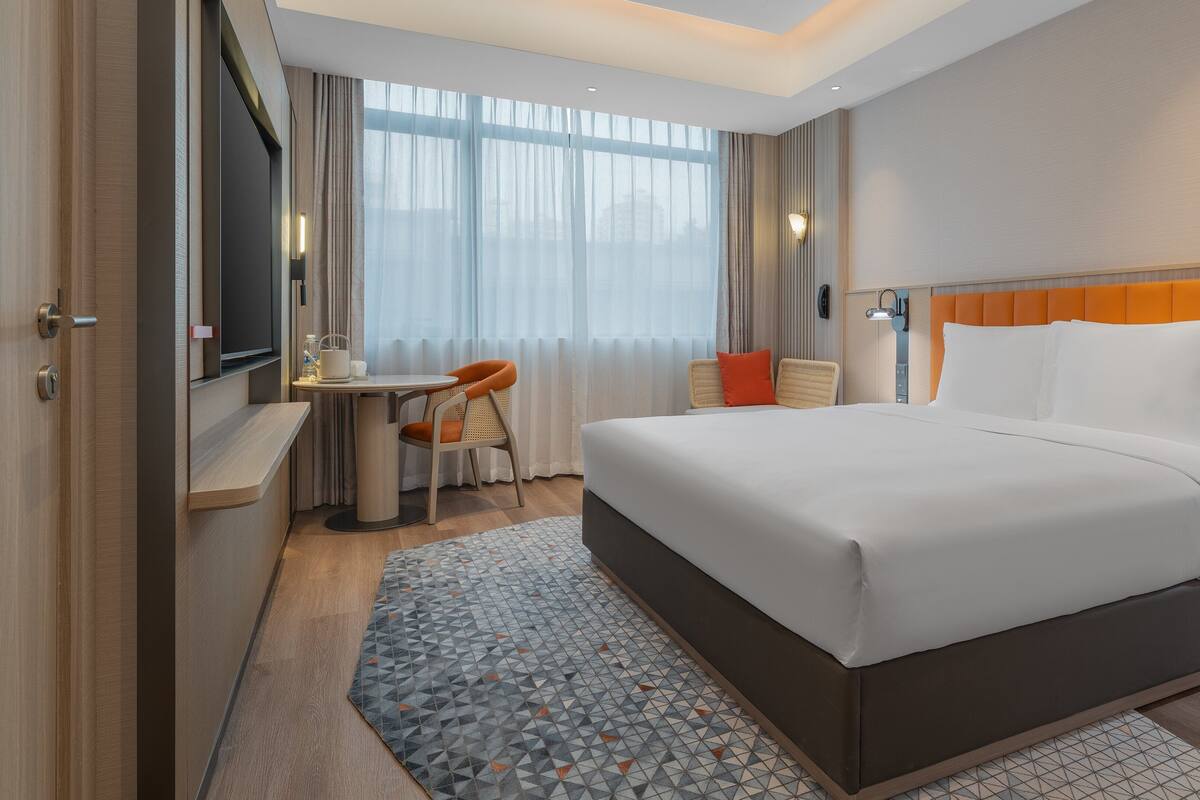 Une chambre d’hôtel comprenant un lit, un bureau, une chaise, une fenêtre avec des rideaux et une lampe fixée au mur.