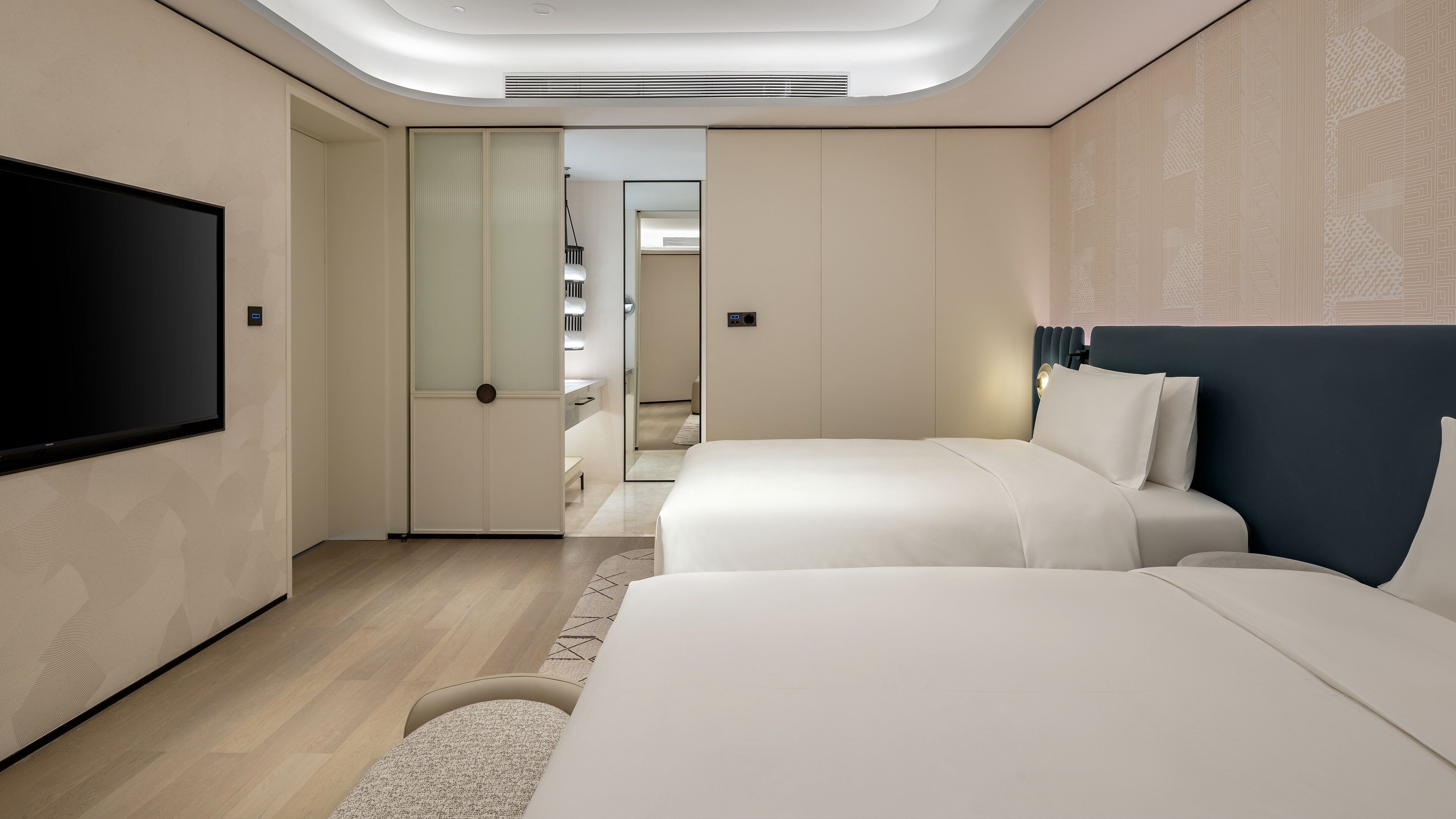Una habitación de hotel moderna con una televisión de pantalla plana, dos camas, un vestidor y un foco en el techo.
