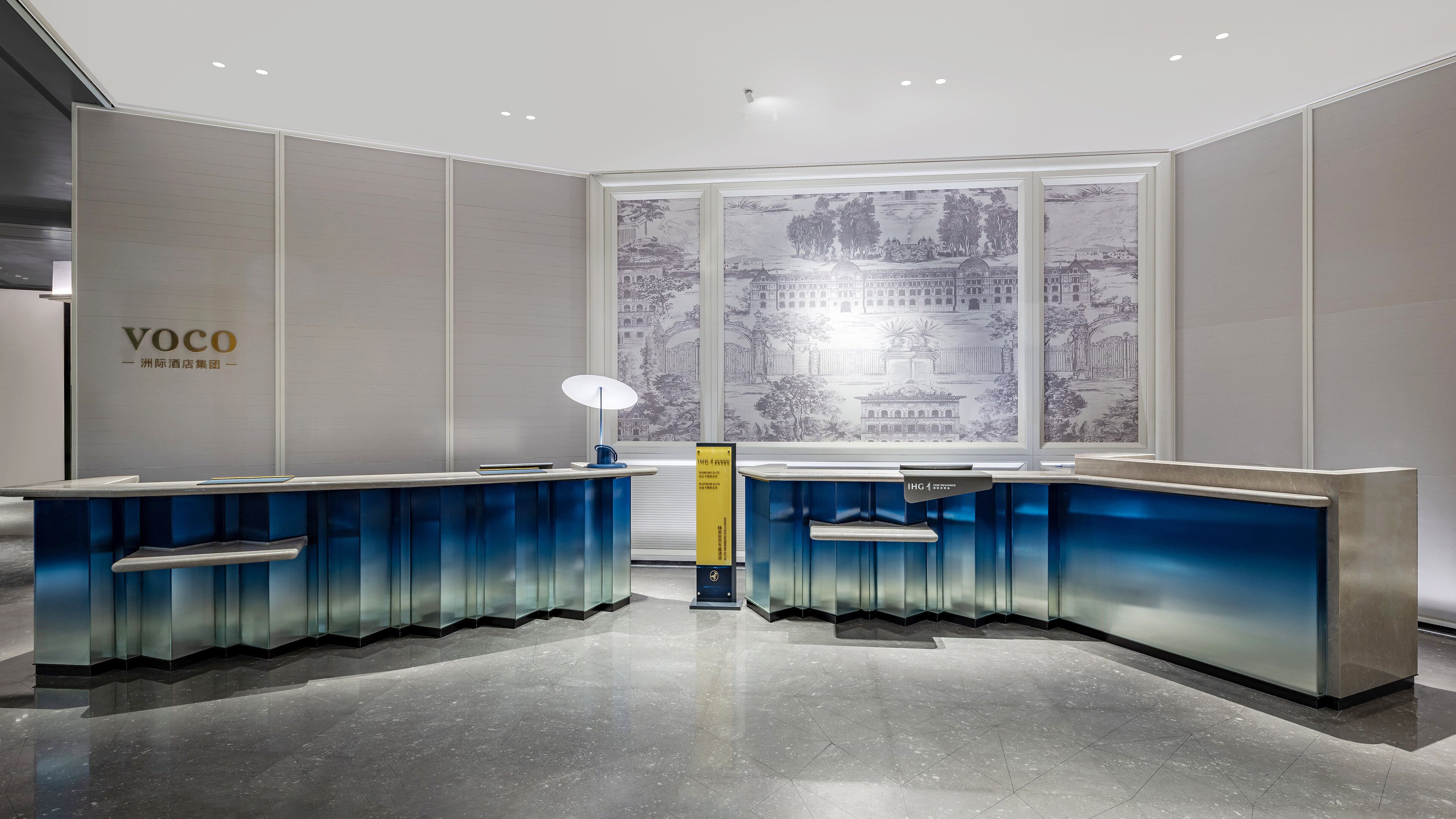 A reception desk with a modern design, a large window with a cityscape view, and a sign indicating the hotel name.