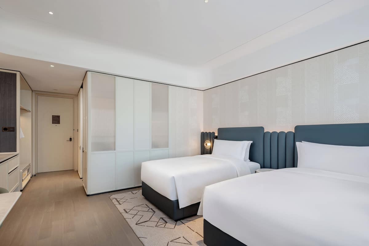 A modern hotel room with two beds, a walk-in closet, and a separate bathroom.