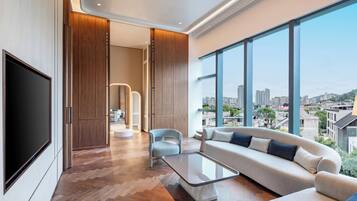 A modern living room with a large TV, a sofa, a coffee table, and a view of the city.