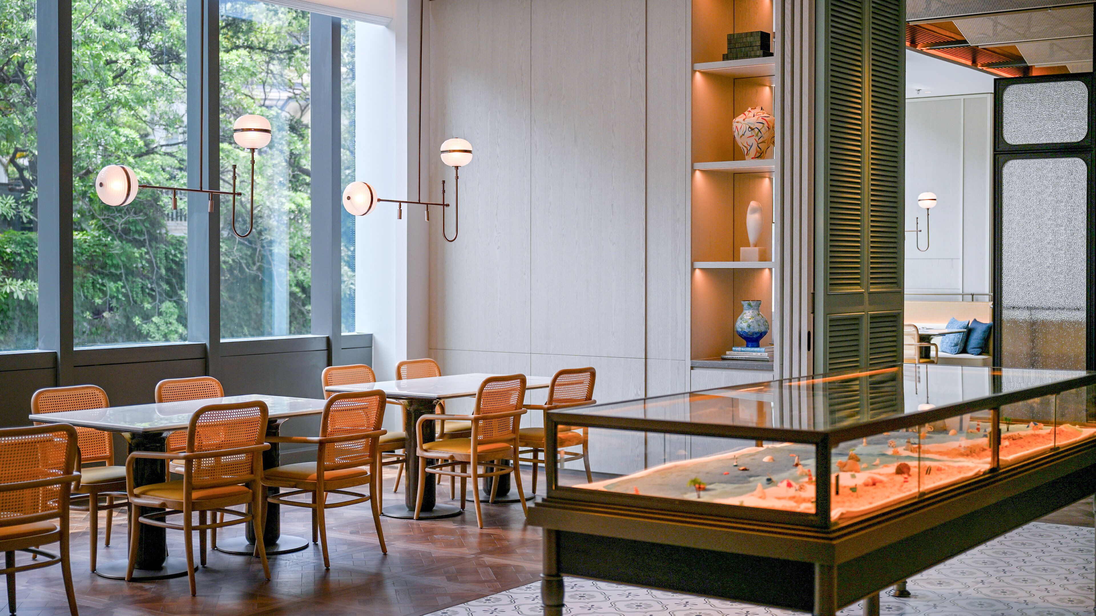 A modern interior with a dining area, large windows, and a display case with a landscape scene.